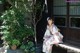 A woman in a kimono sitting on a bench next to a tree.