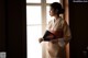 A woman in a kimono standing by a window holding a fan.