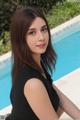 A woman in a black dress sitting by a swimming pool.