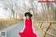 A woman in a red dress and black hat standing on a bridge.