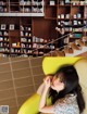 A woman sitting on a yellow chair in front of a book shelf.