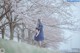 A woman in a blue dress standing in front of a tree.